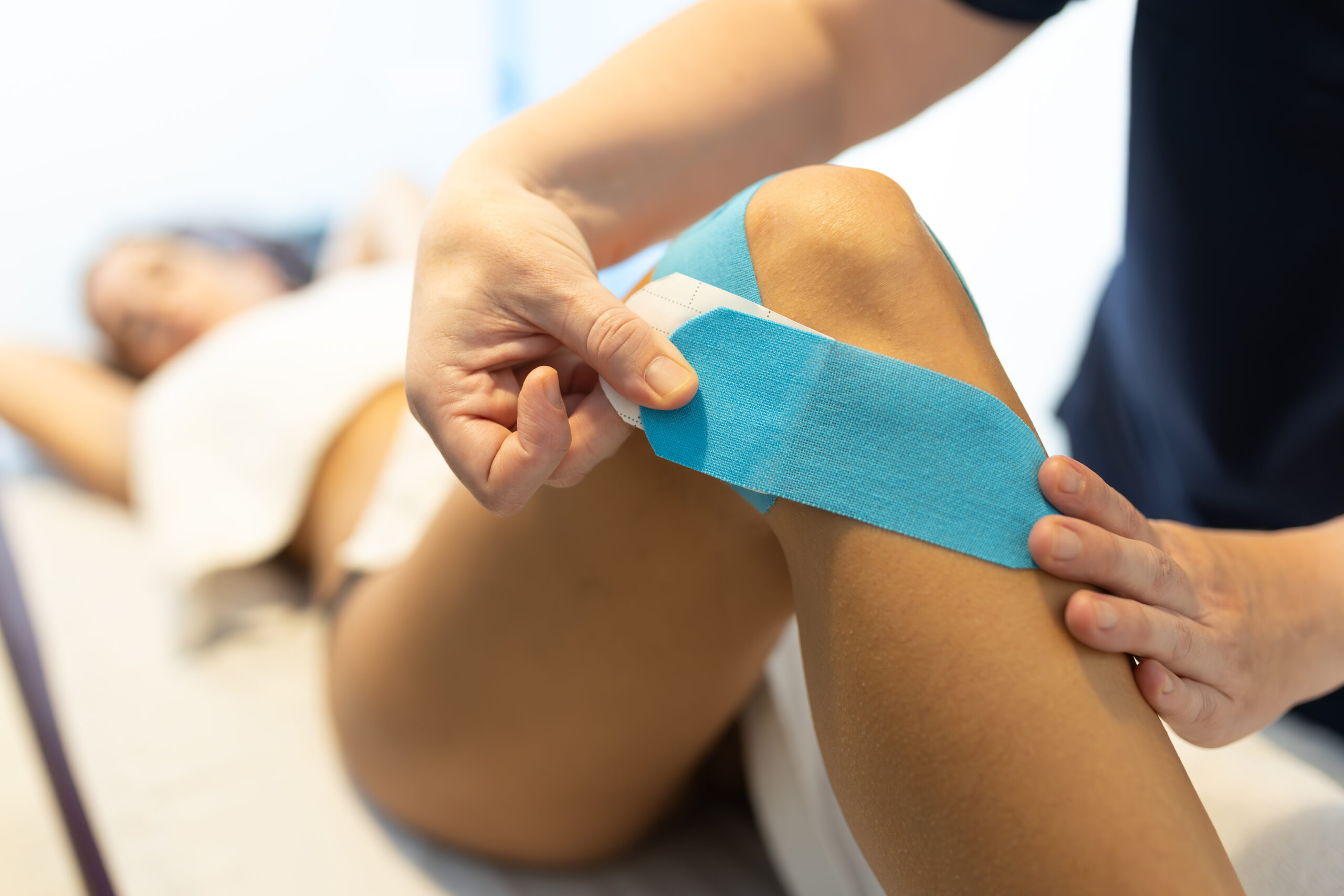 Fisioterapeuta aplicando un vendaje neuromuscular en la rodilla de una paciente, kinesio azul
